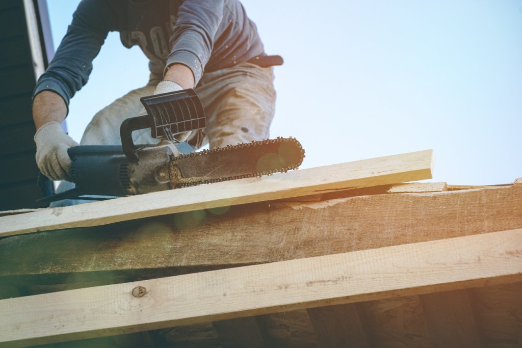 Construction worker safely using a chainsaw on a job site.